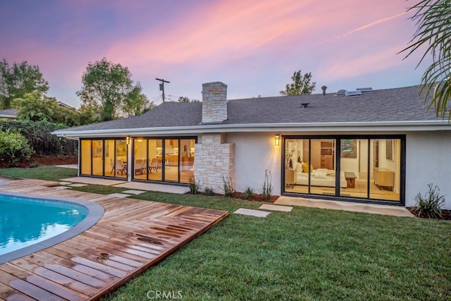 back house at dusk with a lawn and a swimming pool side deck