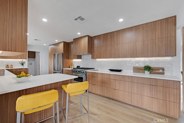 kitchen with wall chimney exhaust hood, a kitchen bar, light hardwood / wood-style floors, decorative backsplash, and high quality appliances