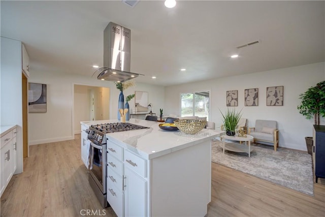 kitchen featuring white cabinetry, a center island, stainless steel gas range oven, light stone countertops, and island exhaust hood