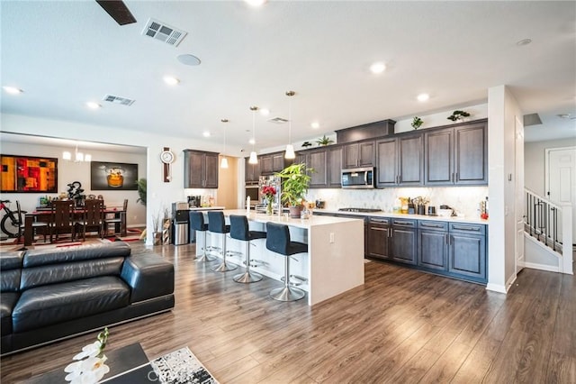 kitchen with hanging light fixtures, a breakfast bar, dark brown cabinetry, and a center island with sink