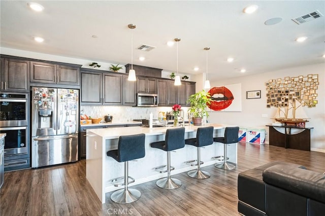 kitchen with pendant lighting, stainless steel appliances, a kitchen island with sink, a breakfast bar, and dark brown cabinets