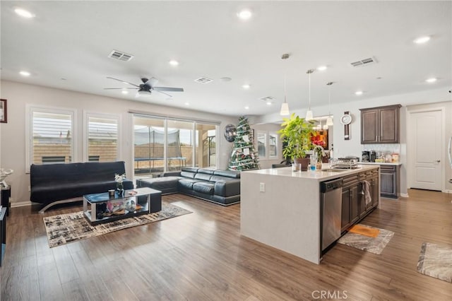 kitchen featuring wood-type flooring, an island with sink, ceiling fan, stainless steel dishwasher, and dark brown cabinets