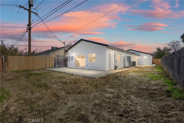 back house at dusk featuring central AC unit, a yard, and a patio