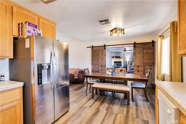 dining area featuring ceiling fan, light hardwood / wood-style floors, and a barn door