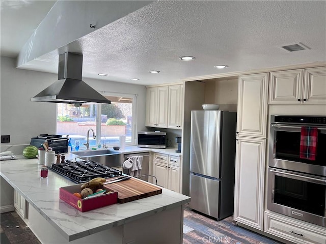 kitchen with island exhaust hood, stainless steel appliances, kitchen peninsula, and light stone countertops