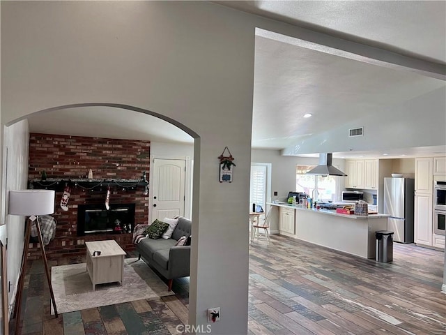 living room featuring a brick fireplace, sink, dark hardwood / wood-style floors, and vaulted ceiling