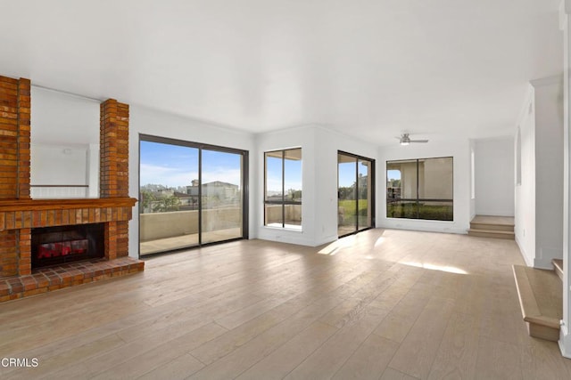 unfurnished living room featuring ceiling fan, light wood-type flooring, and a brick fireplace