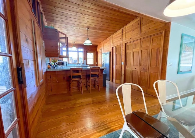 dining area featuring wood walls, wooden ceiling, vaulted ceiling, and light hardwood / wood-style floors