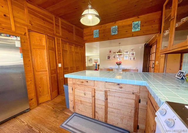 kitchen featuring stainless steel fridge, tile counters, wood walls, and decorative light fixtures