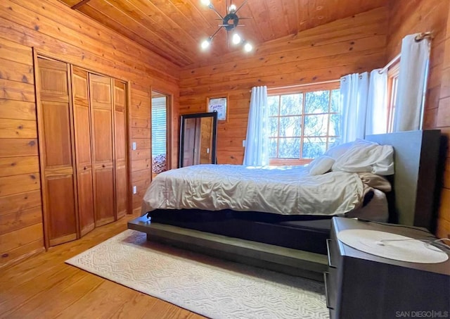 bedroom with lofted ceiling, wooden ceiling, wooden walls, light hardwood / wood-style floors, and a closet