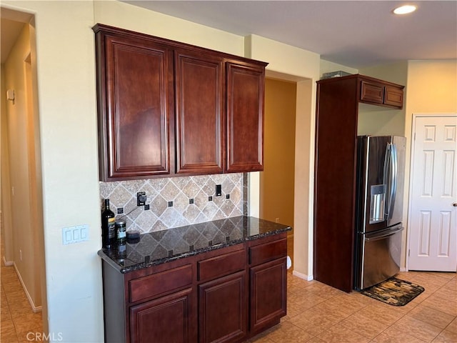 kitchen with stainless steel fridge with ice dispenser, decorative backsplash, and dark stone counters