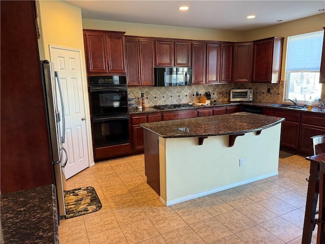 kitchen with sink, dark stone countertops, decorative backsplash, a center island, and black appliances