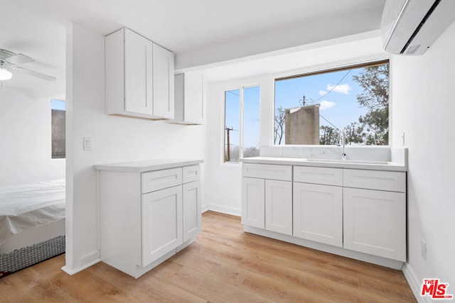 kitchen featuring ceiling fan, an AC wall unit, sink, white cabinetry, and light wood-type flooring