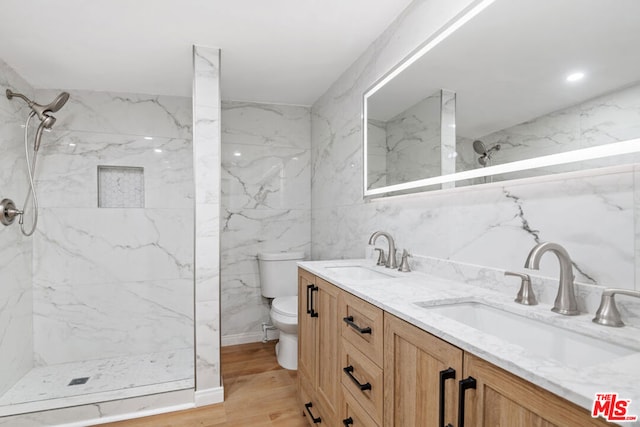 bathroom featuring toilet, a tile shower, hardwood / wood-style flooring, tile walls, and vanity