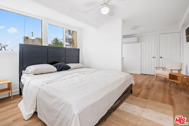 bedroom with a wall unit AC, ceiling fan, and light hardwood / wood-style floors