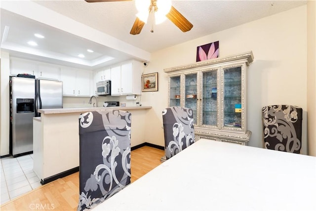 kitchen featuring ceiling fan, appliances with stainless steel finishes, a raised ceiling, white cabinets, and light hardwood / wood-style flooring