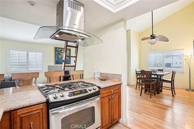 kitchen featuring light hardwood / wood-style floors, island range hood, stainless steel range with gas stovetop, ceiling fan, and light stone countertops