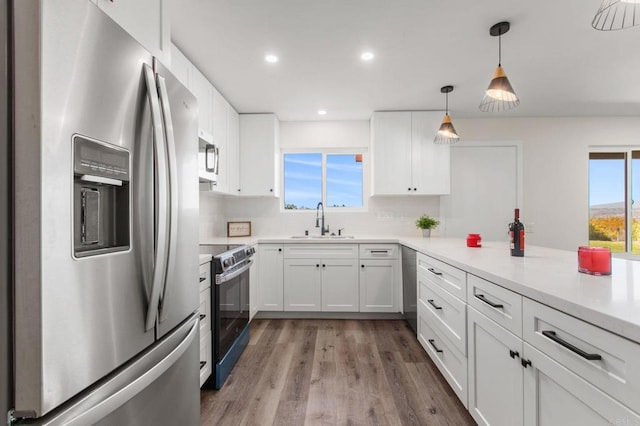 kitchen featuring sink, stainless steel appliances, backsplash, decorative light fixtures, and white cabinets