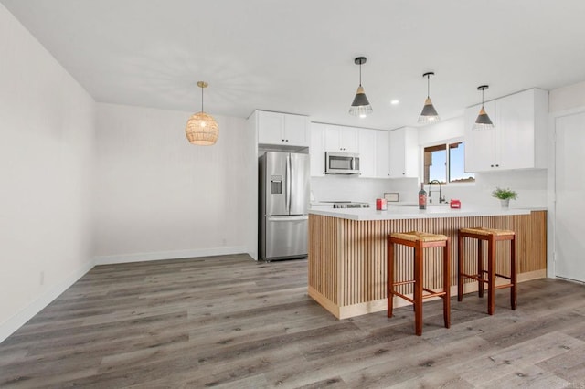 kitchen featuring hardwood / wood-style floors, a breakfast bar area, decorative light fixtures, white cabinetry, and stainless steel appliances