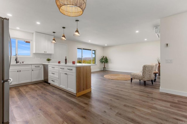 kitchen featuring white cabinetry, hanging light fixtures, kitchen peninsula, stainless steel fridge, and wood-type flooring