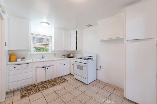 kitchen featuring white range with gas cooktop, light tile patterned flooring, white cabinets, and sink