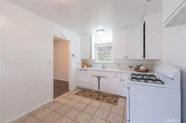 kitchen featuring light tile patterned floors, white gas range, white cabinets, and sink