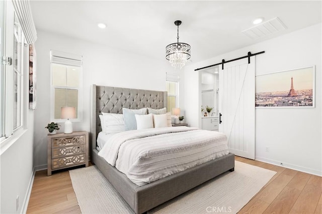 bedroom featuring a barn door, light wood-type flooring, and a notable chandelier