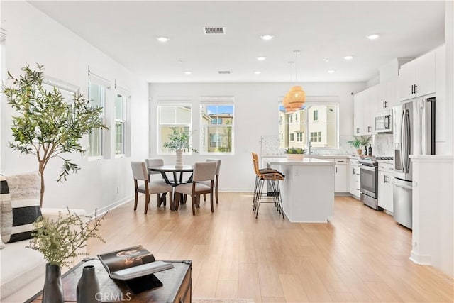 kitchen featuring pendant lighting, white cabinets, a center island, stainless steel appliances, and a breakfast bar area