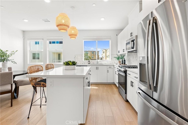 kitchen featuring white cabinets, appliances with stainless steel finishes, a kitchen island, and pendant lighting