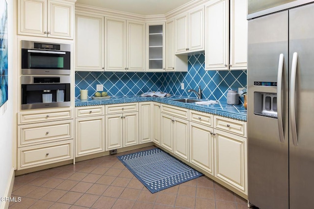 kitchen featuring appliances with stainless steel finishes, tasteful backsplash, sink, light tile patterned floors, and cream cabinetry