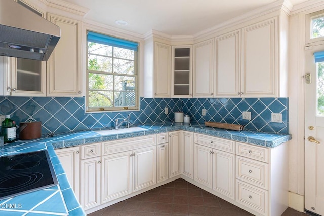 kitchen with dark tile patterned flooring, decorative backsplash, cooktop, cream cabinets, and range hood