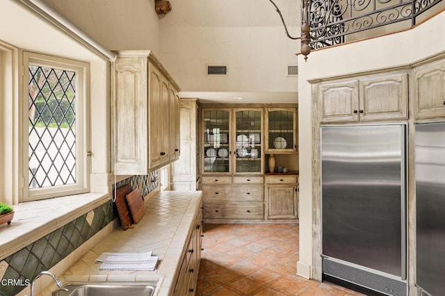 kitchen featuring tile countertops, light brown cabinetry, stainless steel built in refrigerator, and sink