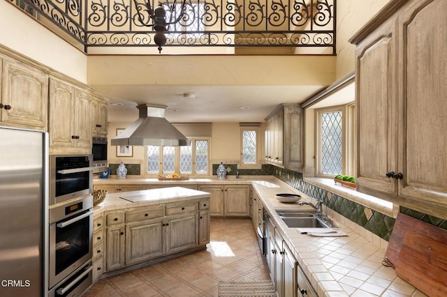 kitchen featuring tile countertops, sink, stainless steel appliances, light brown cabinetry, and island range hood