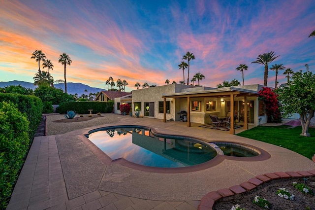 pool at dusk featuring a patio area, a mountain view, and an in ground hot tub