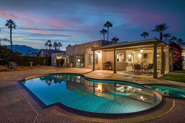 pool at dusk featuring ceiling fan, a patio area, area for grilling, and an in ground hot tub