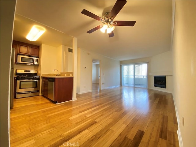 kitchen with a fireplace, appliances with stainless steel finishes, open floor plan, a sink, and light wood-type flooring