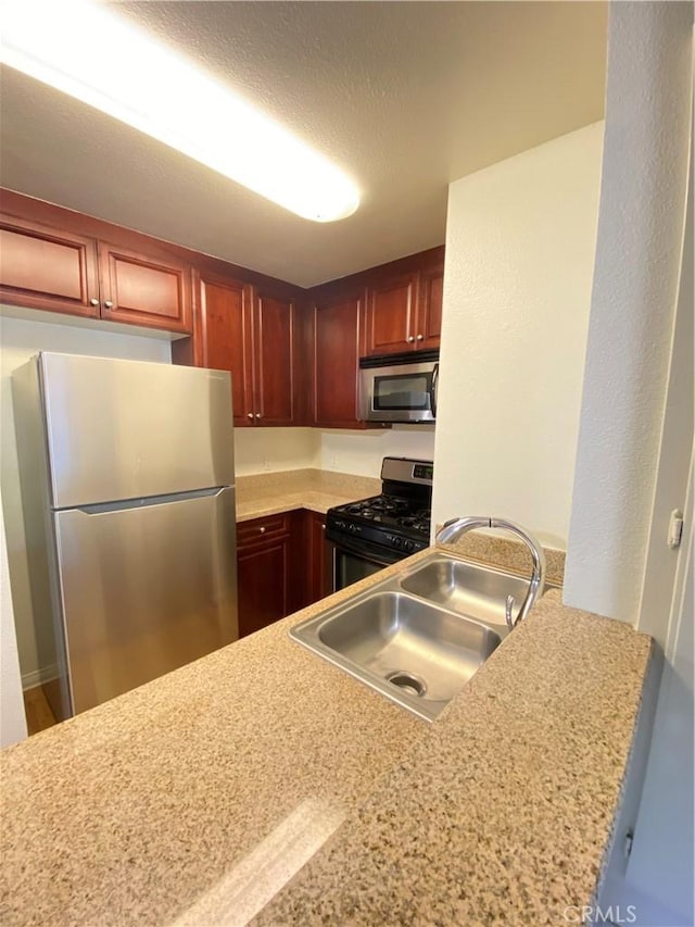 kitchen featuring stainless steel appliances, sink, light stone counters, and kitchen peninsula