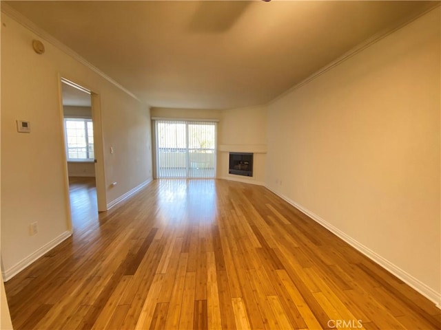 unfurnished living room featuring a wealth of natural light, crown molding, wood finished floors, and a glass covered fireplace