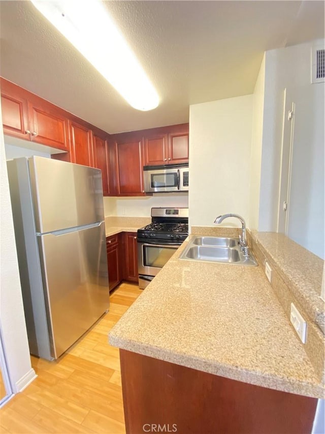 kitchen featuring light wood-style flooring, appliances with stainless steel finishes, a peninsula, light countertops, and a sink