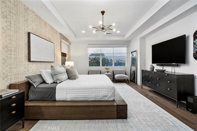 bedroom featuring a raised ceiling, hardwood / wood-style flooring, and an inviting chandelier