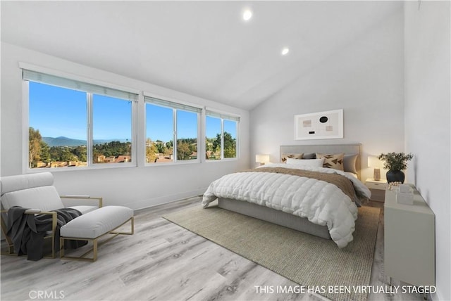 bedroom featuring a mountain view, multiple windows, vaulted ceiling, and light wood-type flooring