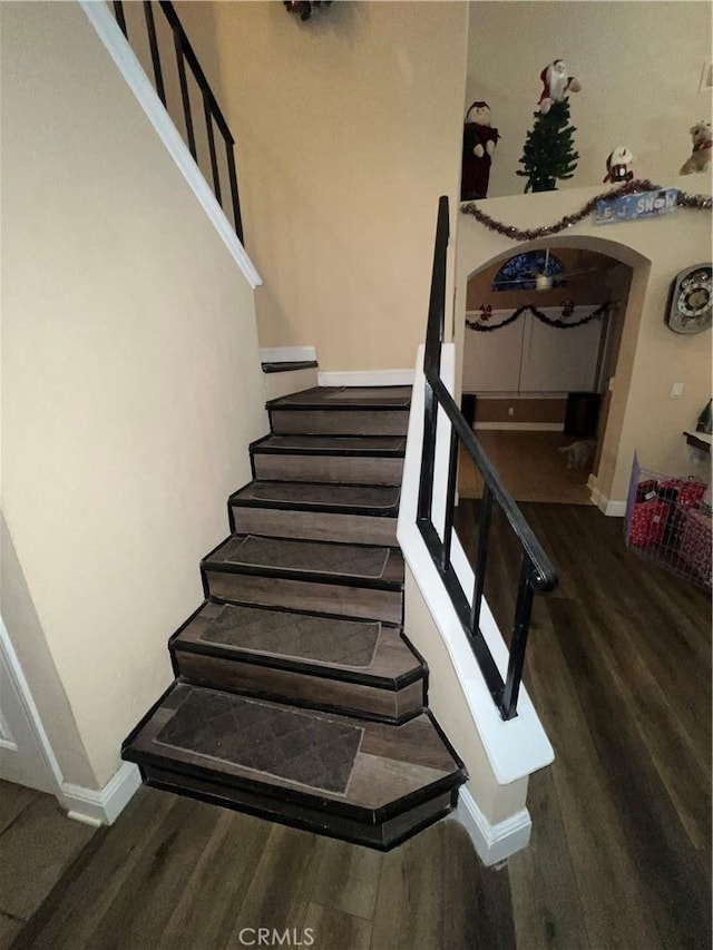 stairs featuring baseboards, arched walkways, and wood finished floors