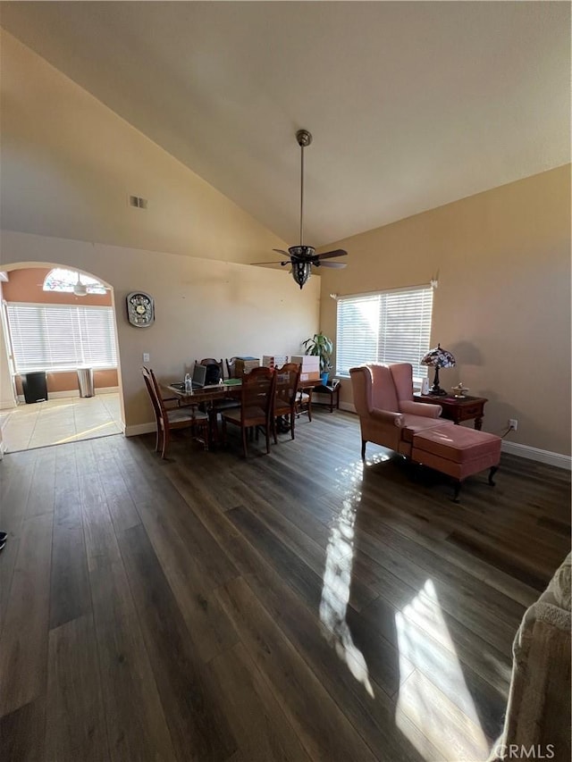 dining space featuring baseboards, arched walkways, a ceiling fan, wood finished floors, and high vaulted ceiling