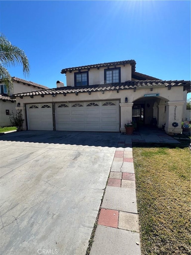 mediterranean / spanish-style house featuring a garage, a tile roof, concrete driveway, and stucco siding