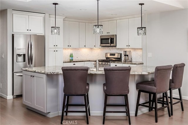 kitchen featuring light stone countertops, appliances with stainless steel finishes, a kitchen island with sink, white cabinets, and dark hardwood / wood-style flooring