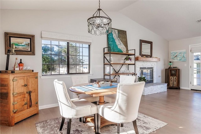 dining space featuring vaulted ceiling, an inviting chandelier, a fireplace, and wood-type flooring