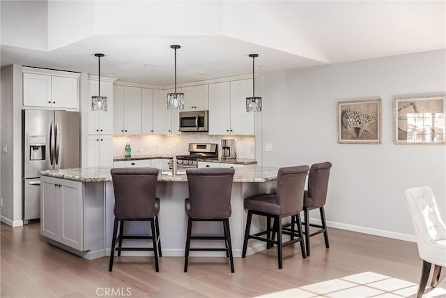 kitchen with light stone countertops, white cabinets, appliances with stainless steel finishes, hanging light fixtures, and a center island with sink