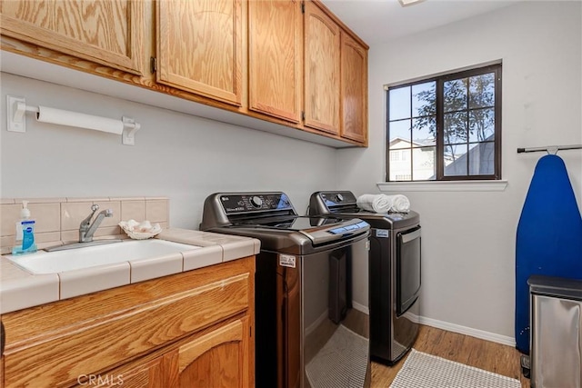 clothes washing area featuring light hardwood / wood-style floors, cabinets, sink, and washing machine and clothes dryer