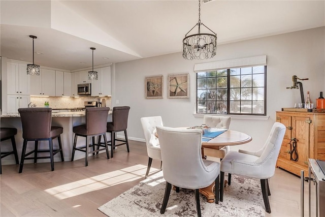 dining room with a chandelier, light hardwood / wood-style flooring, and lofted ceiling