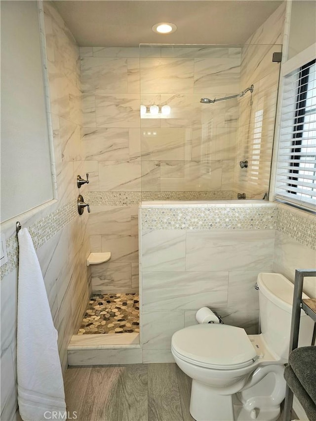 bathroom with toilet, tile walls, a tile shower, and hardwood / wood-style floors